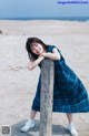 A young girl leaning against a wooden post on the beach.